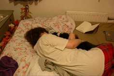 a woman laying in bed with her head on the back of a cat, while reading a book