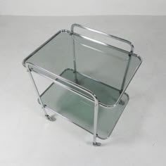 a metal and glass serving cart with wheels on the bottom, sitting on a white surface