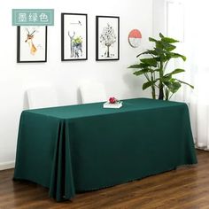 there is a table with a green cloth on it in front of some pictures and a potted plant