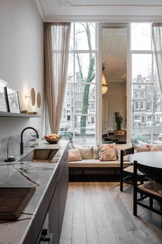 a living room filled with furniture next to a kitchen and dining room table in front of a large window