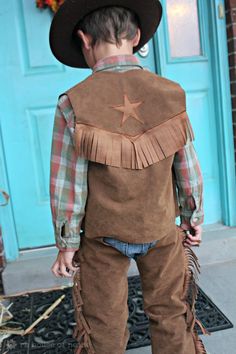 a young boy wearing a cowboy outfit and hat standing in front of a blue door