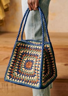 a woman is holding a crocheted bag in her right hand while standing on a wooden floor