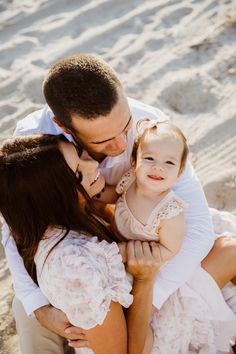 a man and woman holding a baby in their arms on the sand at the beach