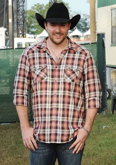 a man wearing a cowboy hat standing in the grass with his hands in his pockets