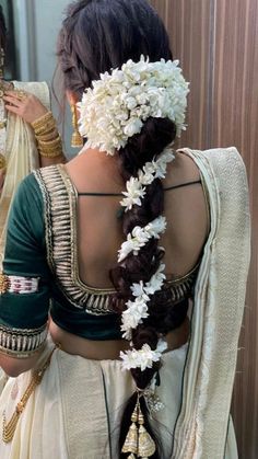 a woman with flowers in her hair wearing a white sari and holding a mirror