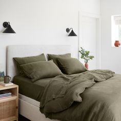 a bed with green sheets and pillows in a white room next to an open window