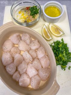 a bowl filled with raw chicken next to lemons and parsley