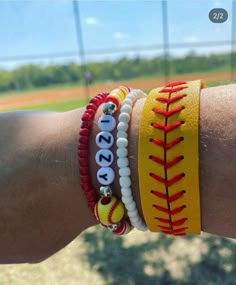 a person's arm with three bracelets on it and a baseball in the background