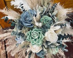 an arrangement of flowers and feathers is displayed on a wooden table with wood boards in the background