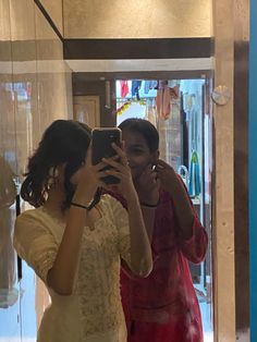 two women standing in front of a mirror looking at their cell phones and taking pictures