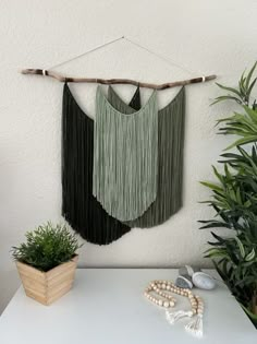 a wall hanging with two green fringes on it next to a potted plant