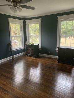 an empty room with hard wood floors and blue walls, two windows on the far wall