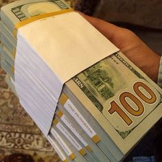 a person is holding stacks of money in their left hand, with one hundred dollars on the other