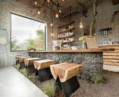 a restaurant with stone walls and wooden benches in front of the counter, surrounded by greenery