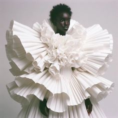 a woman in a white dress made out of folded up paper petals, with her hands on her hips