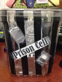 a cell phone in a plastic container on a wooden table with a prison cell sticker attached to it