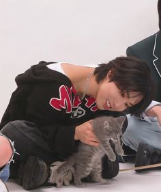 a young man holding a kitten while sitting on the floor next to two other people