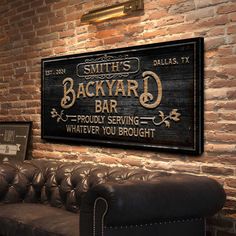 the back yard bar sign is mounted on a brick wall above a leather couch in an old - fashioned restaurant