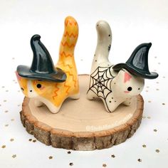 three ceramic cats wearing witches hats on top of a wooden slice with gold stars in the background