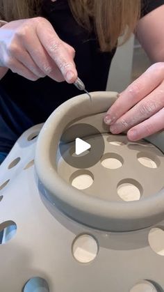 a woman is making a vase out of clay with her hands on the wheel and holding a knife