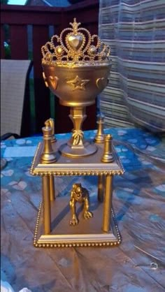 a golden trophy with a crown on top sitting on a table in front of a fence