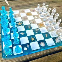 a glass chess board with shells and starfishs on it, sitting on a wooden table