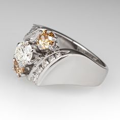 This lovely three-stone diamond ring is centered with one (1) round brilliant cut diamond set into a six- prong setting and flanked to each side by one (1) old European cut fancy light brown colored diamond set into a six-prong setting. The shoulders of the ring are accented with diamonds. One shoulder is bead set with nineteen (19) round single cut diamonds and one (1) round brilliant cut diamond. The other shoulder is channel set with five (5) round brilliant cut diamonds. The ring measures 13.1mm at the top, rises 6.8mm above the finger, tapering to 2.9mm wide and 1.1mm thick at the base of the shank. It is currently a size 6. Several of the diamonds are lightly chipped. Brown Prong-set Ring For Anniversary, Brown Prong Set Ring For Anniversary, Brown Rings With Prong Setting For Anniversary, Elegant Brown Diamond Ring For Formal Occasions, Elegant Brown Diamond Ring, Brown Diamond Ring Fine Jewelry, Brown Diamond Ring With Diamond Accents For Anniversary, Brown Diamond Ring With Accents For Anniversary, Elegant Brown Diamond Round Ring