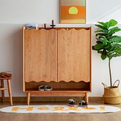 a wooden cabinet sitting on top of a hard wood floor next to a potted plant