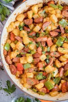 a pan filled with sausage and vegetables on top of a table next to utensils