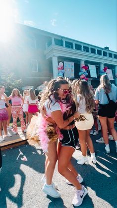 two young women hugging each other in front of a group of people wearing pink and white outfits