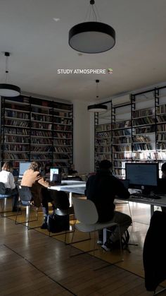 people are sitting at desks in front of bookshelves with computers on them