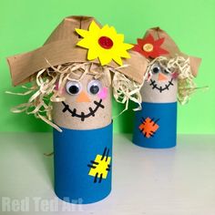 two scarecrows made out of toilet paper tubes with straw on the top and one wearing a sunflower hat