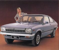 a woman leaning on the hood of a car in front of a red wall with her arms crossed