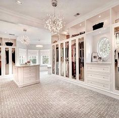 a large walk in closet filled with lots of white cabinets and drawers next to a chandelier