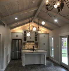 an empty kitchen with wood floors and white cabinets, chandelier hanging from the ceiling