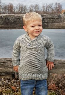 a little boy standing next to a wooden fence with his hands in his pockets and smiling at the camera