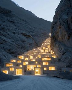 the building is lit up at night in front of some mountains and rocks with lights shining on it