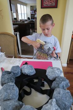 a young boy decorating a birthday cake with gray rocks and black ribbon around the edges