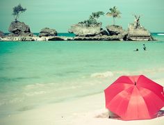 a red umbrella sitting on top of a sandy beach next to the ocean with people in the water