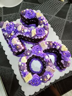 three decorated chocolate donuts sitting on top of a white doily with purple frosting