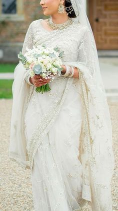 a woman in a white sari holding a bouquet of flowers and wearing a veil