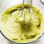 a mixing bowl filled with green cream and two metal whisks in it's center