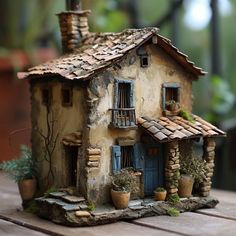 a doll house made out of clay sitting on top of a wooden table next to potted plants