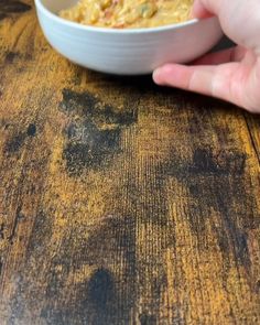 a person holding a bowl of food on top of a wooden table