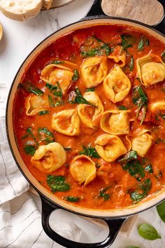 a pot filled with pasta and sauce on top of a white table next to bread