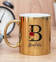 a gold coffee mug sitting on top of a wooden table next to an alarm clock