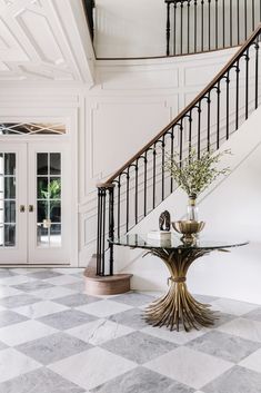 a foyer with marble flooring and white walls, black iron railings and a glass top table