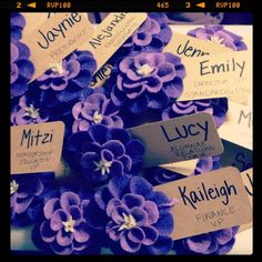 purple flowers with name tags on them are arranged in a pile, ready to be used as an ornament