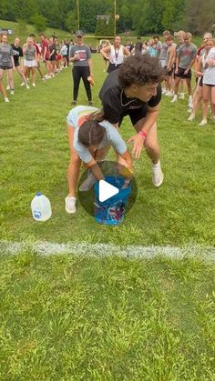 two girls are bending over to pick up a frisbee on the field while others watch