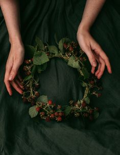 two hands are holding a wreath made out of leaves and berries on a green sheet